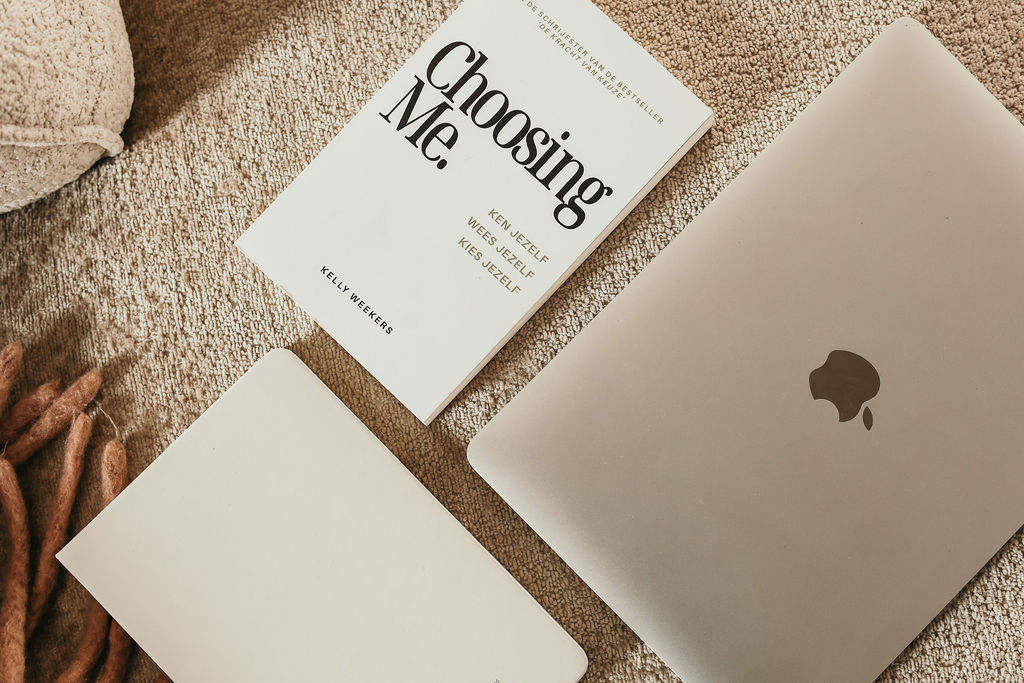 Boek ‘Choosing Me’ van Kelly Weekers, een notitieboek en MacBook op een zachte ondergrond – inspiratie voor persoonlijke groei en reflectie