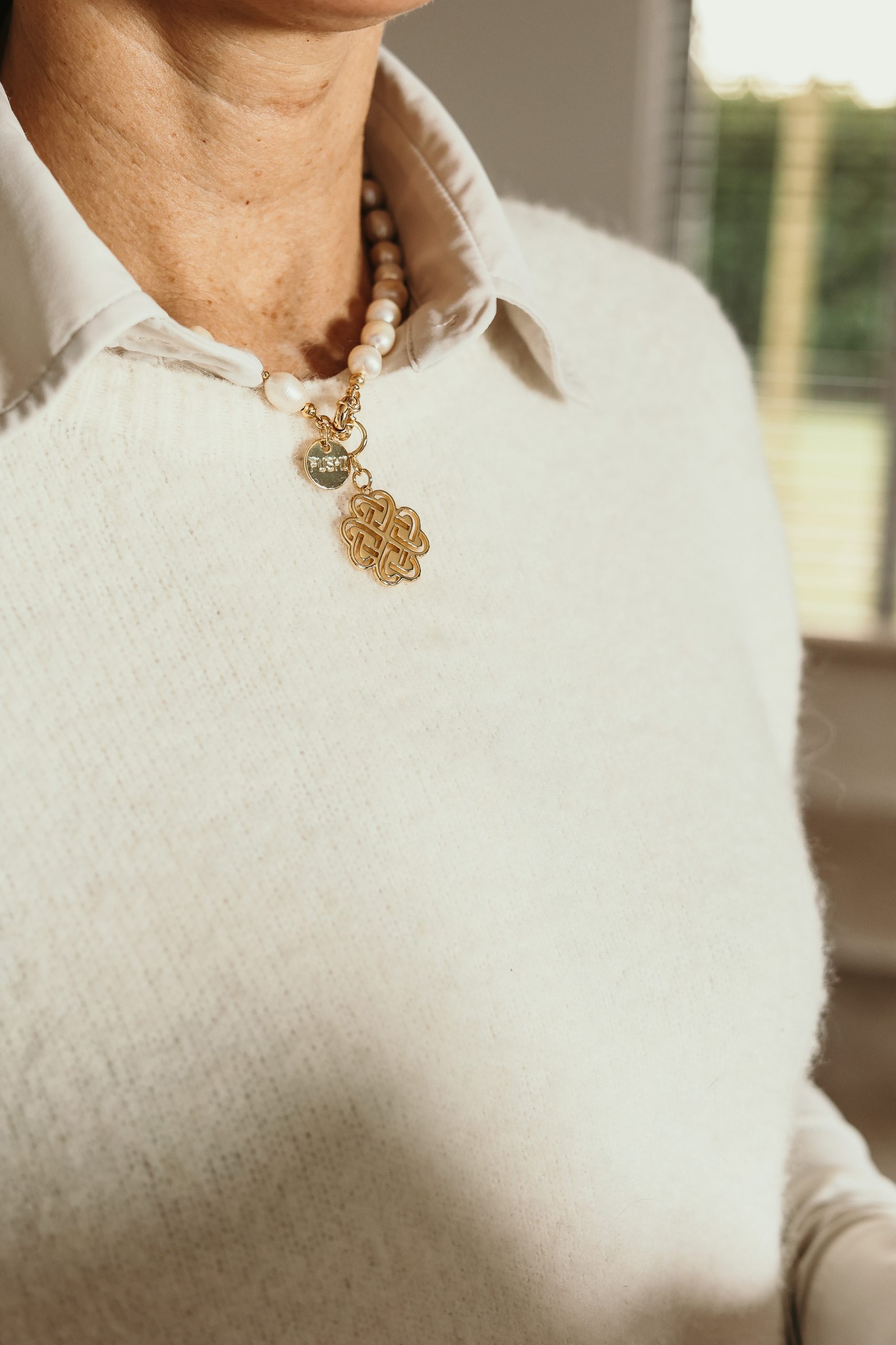 Dianne Verkerk Detail van een parelketting met gouden hanger in de vorm van een oneindige knoop, symbool voor verbinding, kracht en betekenis in persoonlijke groei.